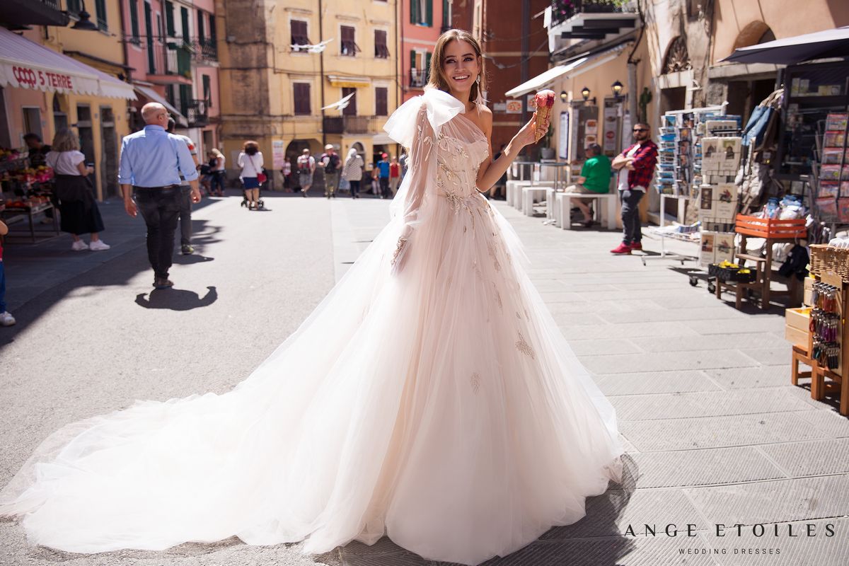 Rara Avis fluffy light train wedding dress Gretta with a left shoulder decorated with a detachable bow at Dell'Amore Bridal, NZ. 1