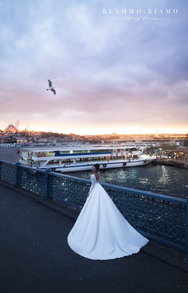 A bride wearing satin princess wedding dress Tilda by blammo-biamo with long sleeves, long train and open back with brooch by Rara Avis at Dell' Amore Bridal, Auckland, NZ. 3