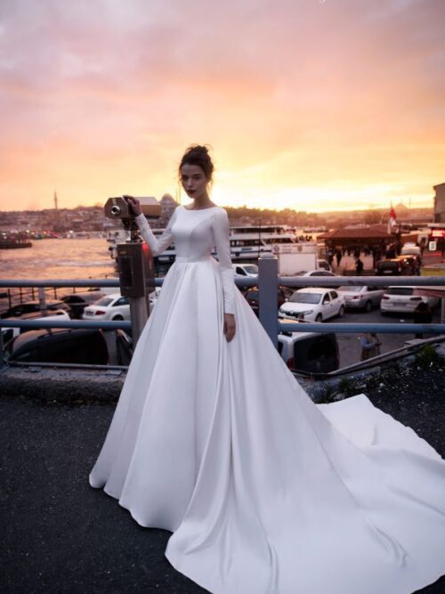 A bride wearing satin princess wedding dress Tilda by blammo-biamo with long sleeves, long train and open back with brooch by Rara Avis at Dell' Amore Bridal, Auckland, NZ. 4